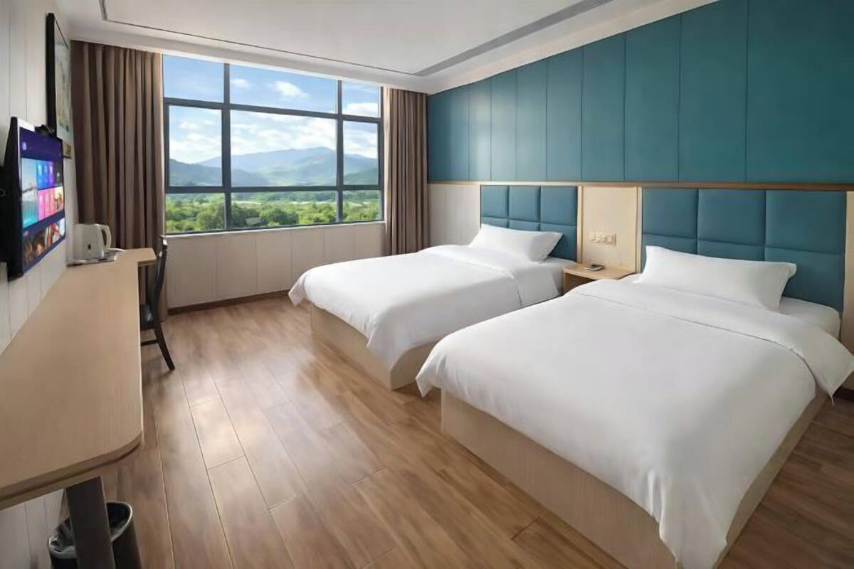 A hotel room with two beds, a desk, a TV, and a window with a mountain view.