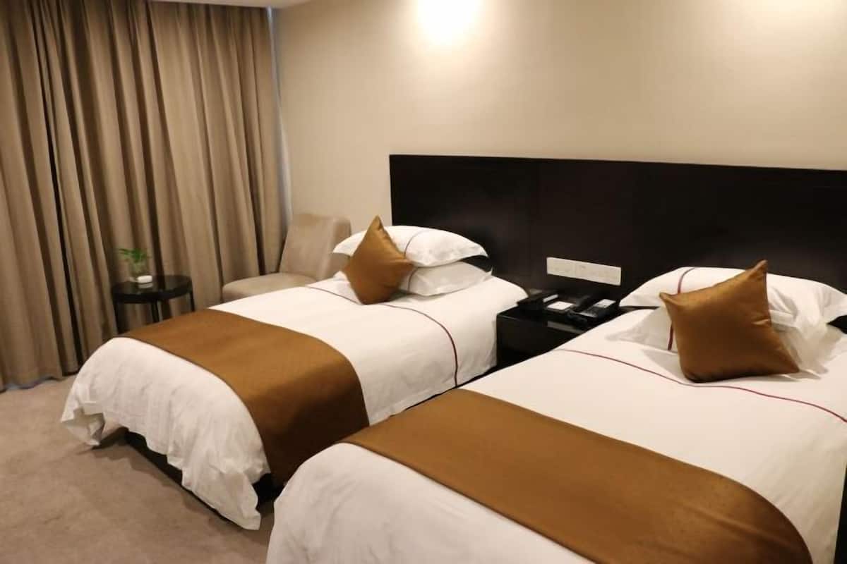 Habitación de hotel con dos camas, cabecera, mesita de noche y cortina.