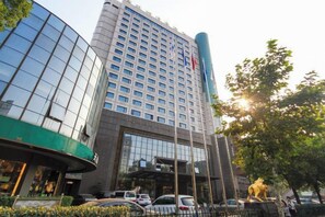 Un hotel a più piani con un ingresso imponente, una grande facciata vetrata e una statua sullo sfondo.