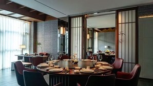 A modern dining area with a round table set for six, surrounded by red chairs. - Hangzhou Bay Hotel (Hangzhou)