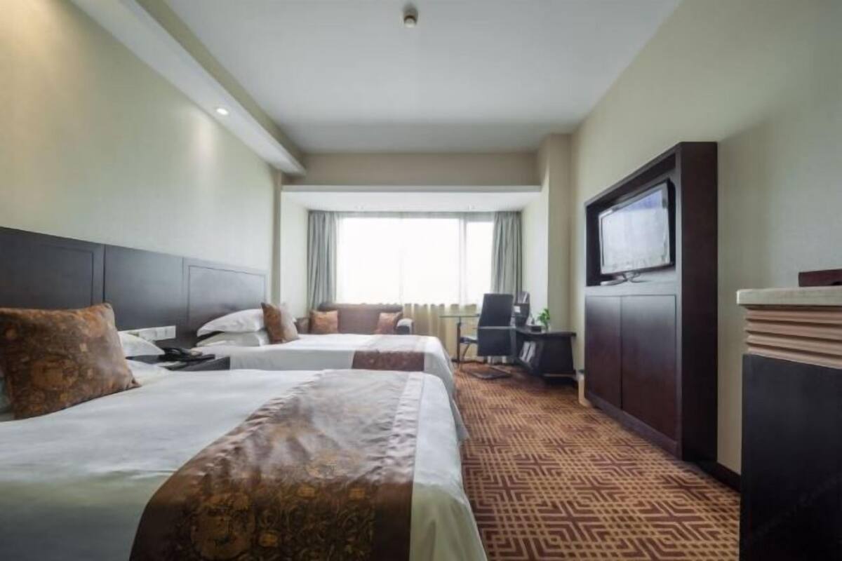 Una habitación de hotel con dos camas, un escritorio, un televisor y una alfombra estampada.