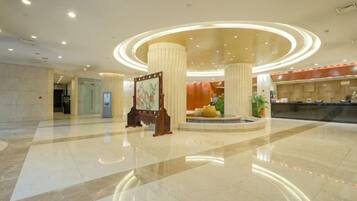 Un vestíbulo de hotel con una recepción, un cuadro grande sobre un atril y una lámpara circular en el techo.