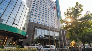 A modern hotel with a glass facade, a prominent flag, and a statue of a lion. - Hangzhou Bay Hotel (Hangzhou)