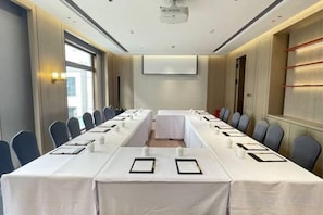 Una sala conferenze con un lungo tavolo, sedie, uno schermo per proiettore e una lavagna.