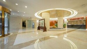 A modern hotel lobby with a reception desk, a central column, and a glass elevator. - Hangzhou Bay Hotel (Hangzhou)