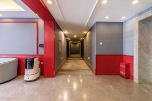 Un pasillo de hotel con una máquina de café, un cesto de basura y una puerta a la derecha.