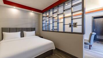 A hotel room with a large bed, a nightstand, a wall-mounted TV, and a window with a view of the outside.