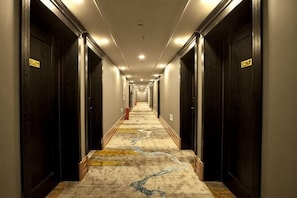 A long, narrow hotel corridor with dark wooden doors on either side and a carpeted floor. - Reese Hotel (Beijing)