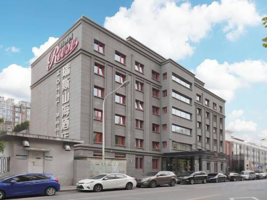 A multi-story hotel with a prominent sign, a covered entrance, and a row of parked cars.