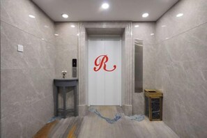 An elevator with a red 'R' on the door, a small table with a sink, and a trash bin. - Reese Hotel (Beijing)