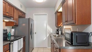 A compact kitchen with wooden cabinets, a stainless steel refrigerator, a microwave, and a gas stove. - Charming 2-bedroom, queen-bed, townhome in the center of Lafayette with AC, WiFi (Lafayette)