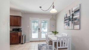 A dining area with a white table and chairs, a potted plant, and a view through a glass door. - Charming 2-bedroom, queen-bed, townhome in the center of Lafayette with AC, WiFi (Lafayette)