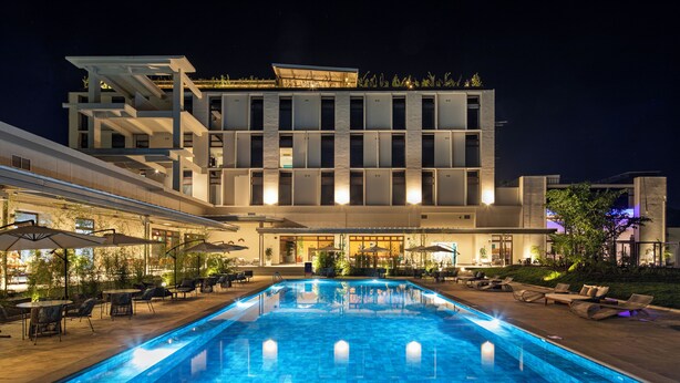 A modern hotel with a swimming pool, outdoor seating, and a well-lit facade.