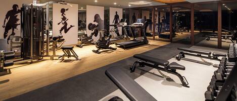 A modern gym with various exercise equipment, including treadmills, elliptical machines, and weight stations.