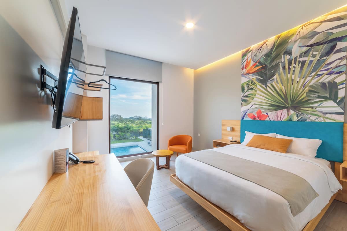 Une chambre d’hôtel moderne dotée d’un grand lit, d’un bureau, d’une chaise, d’un téléviseur fixé au mur et d’une grande fenêtre donnant sur l’extérieur.