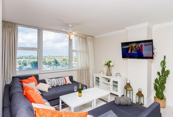 Relax in this stylish living room with a large window offering a view of the surrounding landscape, a ceiling fan, and a flat-screen TV.