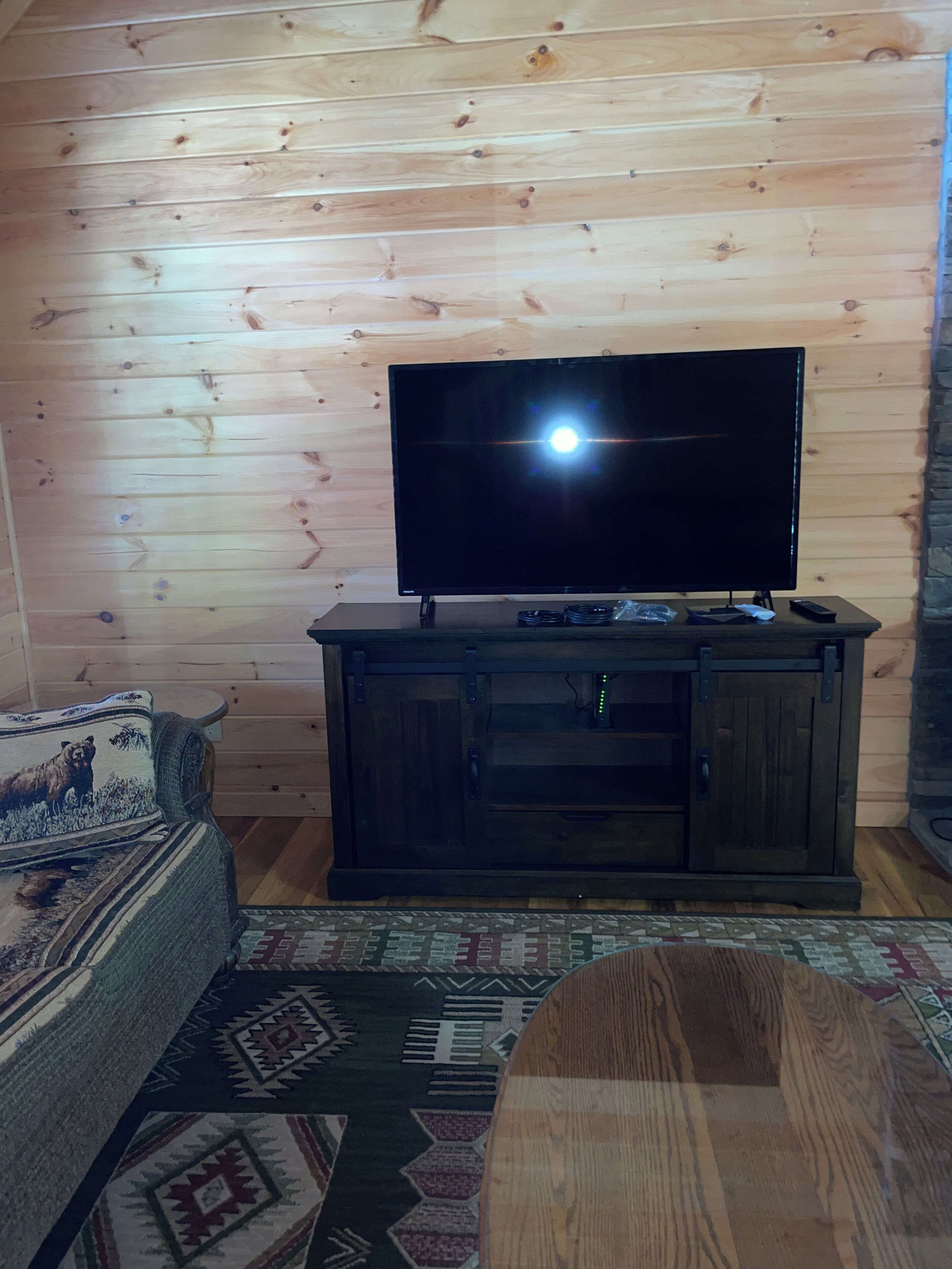 A wooden-paneled room with a television on a dark wooden stand, a patterned rug, and a couch with a cushion.