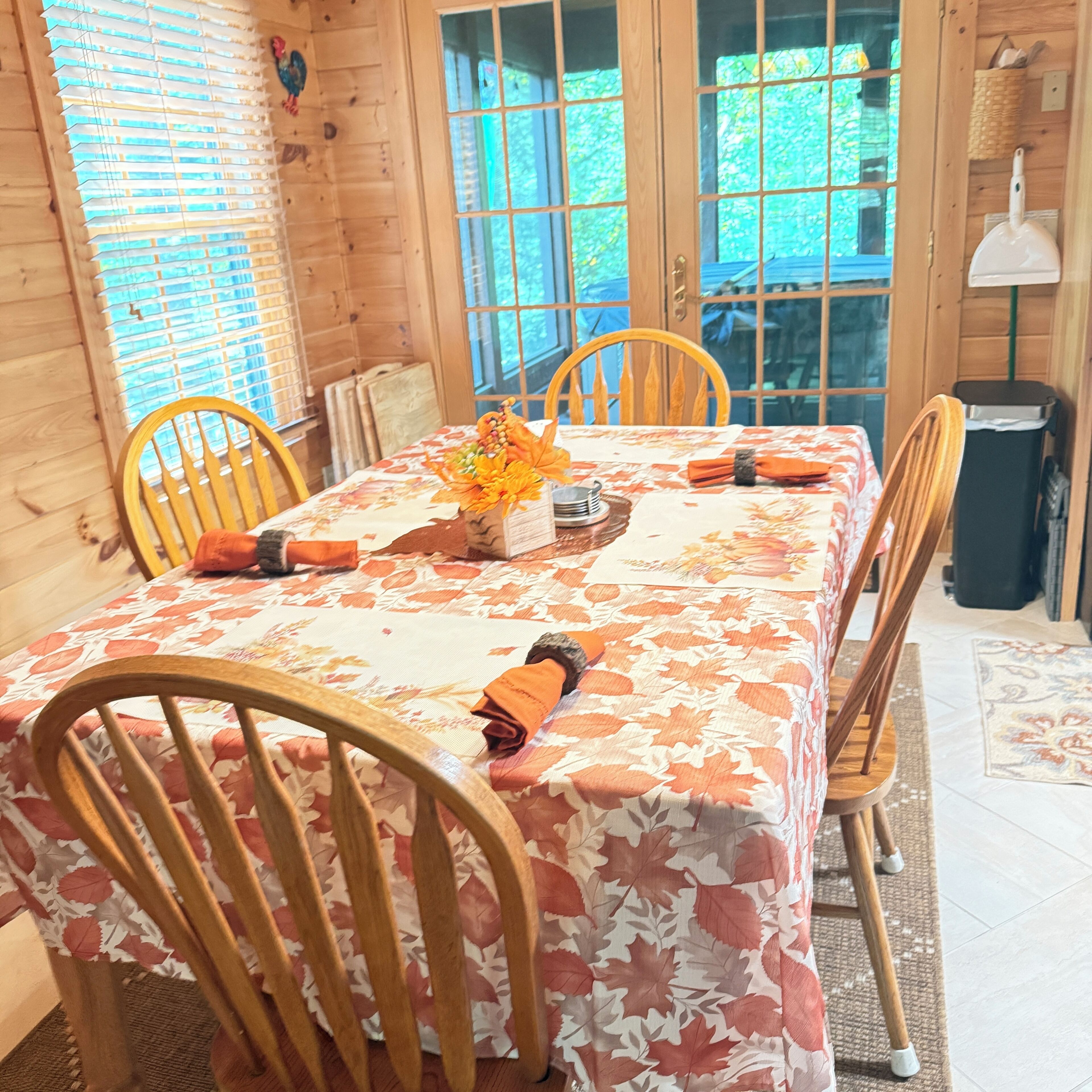 Une table à manger en bois, avec des chaises, une nappe à motifs floraux et un vase rempli de fleurs oranges.