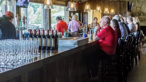 A bar area with a long counter, multiple wine bottles, and glasses. There are hanging lights and a television screen above the bar. - Look NO Further - Hot Tub, 6 miles from Cades Cove (Townsend)