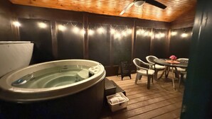 Een hottub in een houten kamer met een plafondventilator, een tafel met stoelen en een klein mandje op de vloer.