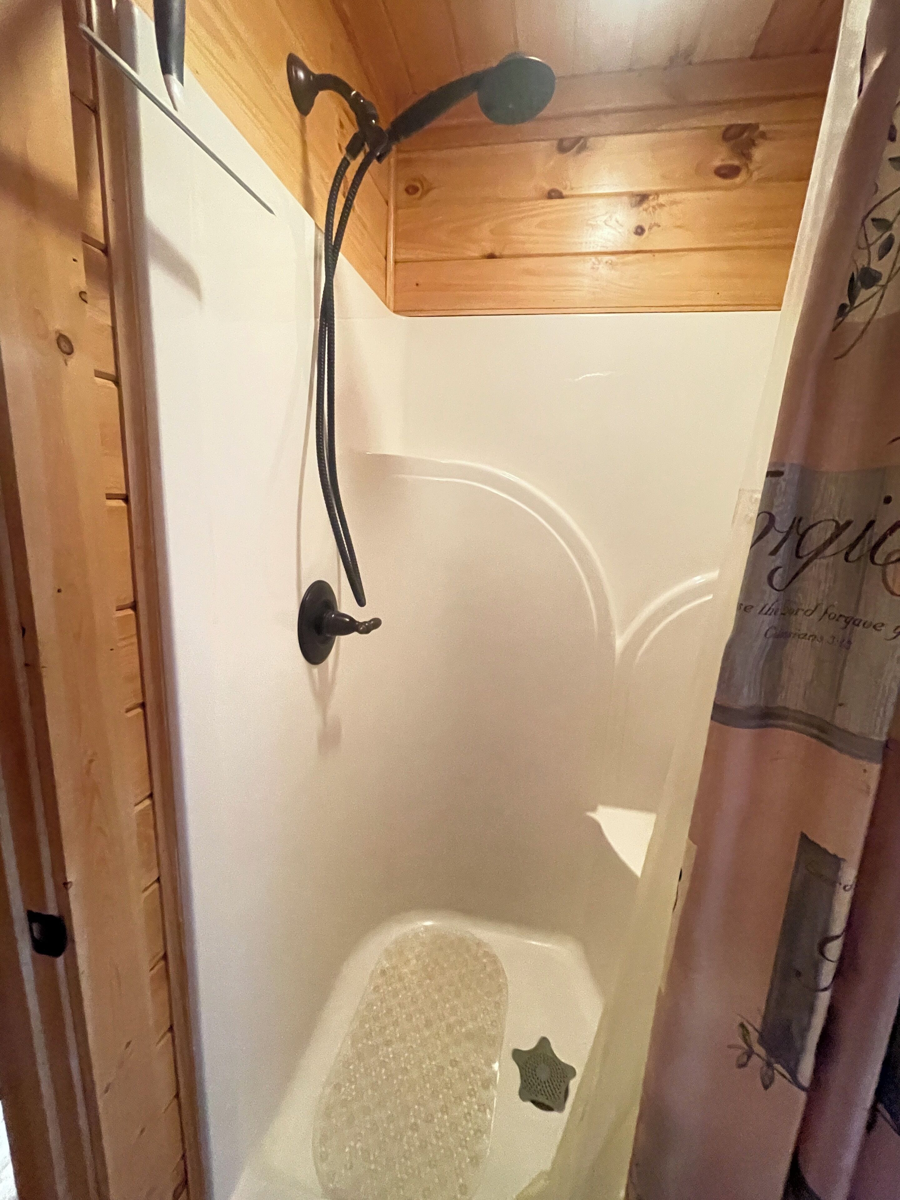 A wooden cabin bathroom with a shower, a bathtub, and a curtain with floral patterns.