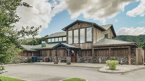 A rustic lodge with a stone foundation, large windows, and a prominent front porch. - Look NO Further - Hot Tub, 6 miles from Cades Cove (Townsend)