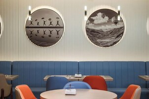 Un restaurante con área de asientos en una cabina azul, mesas redondas y obras de arte colgadas en la pared.