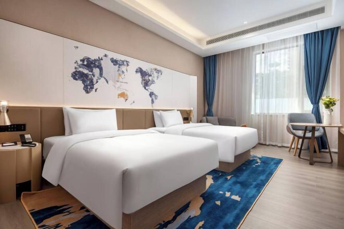 Hotellihuone, jossa on kaksi sänkyä, työpöytä, tuoli, seinällä maailmankartta ja suuri ikkuna, jossa on verhot.