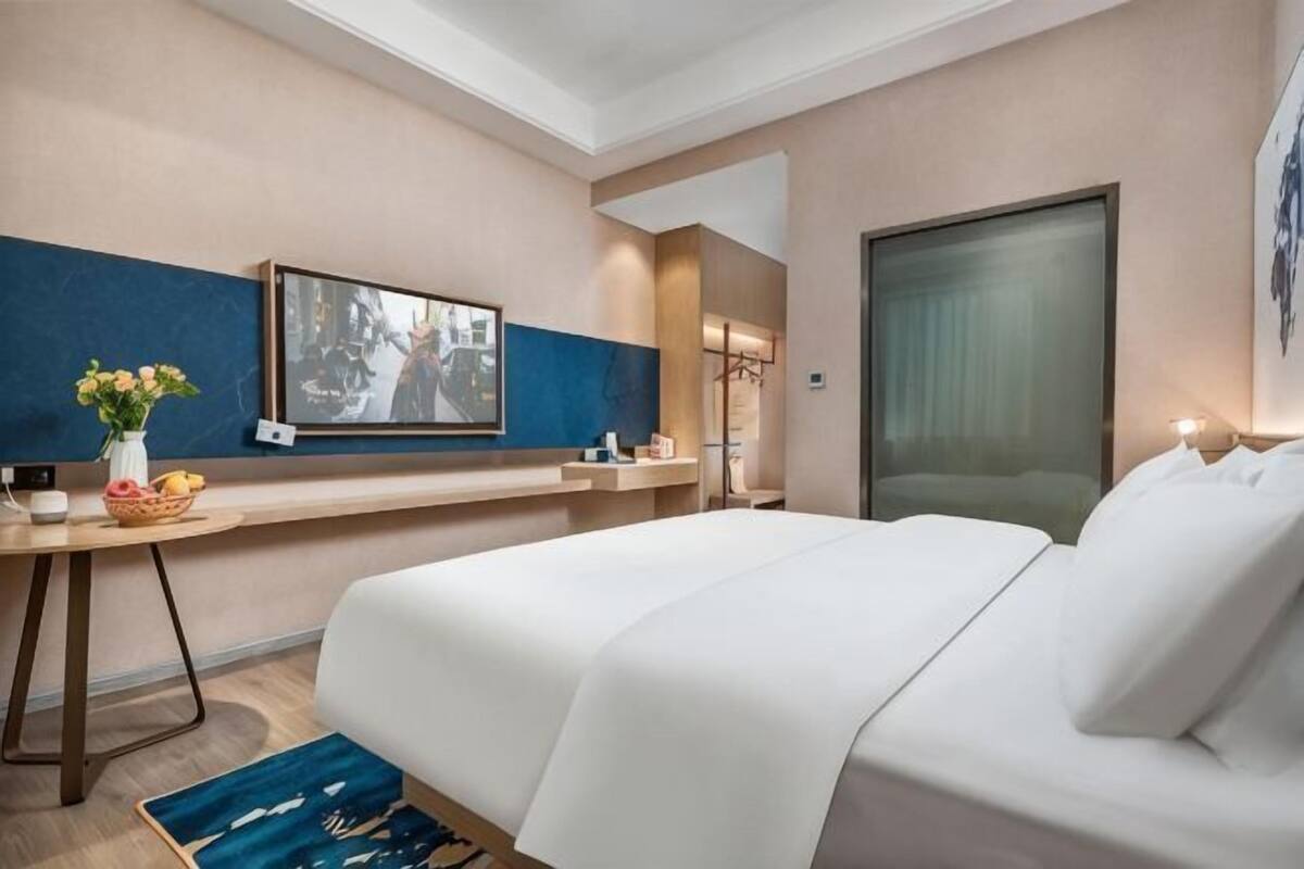 Hotellihuone, jossa on sänky, kirjoituspöytä maljakkoineen, televisio ja suuri ikkuna.