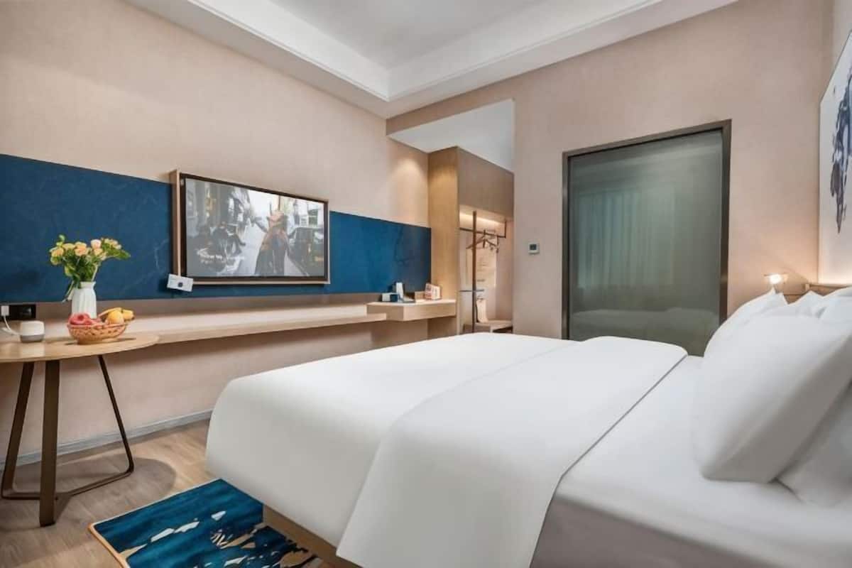 A hotel room with a bed, a desk with a vase of flowers, a television, and a large window.