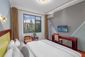 Ein Hotelzimmer mit Bett, Schreibtisch, Stuhl, Fernseher und einem Fenster mit Vorhängen.