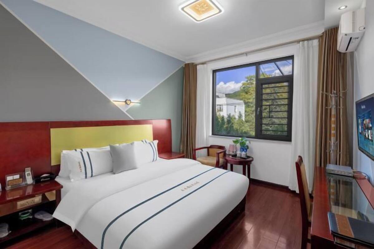 Une chambre d’hôtel équipée d’un lit, d’un bureau, d’une chaise, d’une fenêtre donnant sur un paysage agréable et d’un luminaire au plafond.