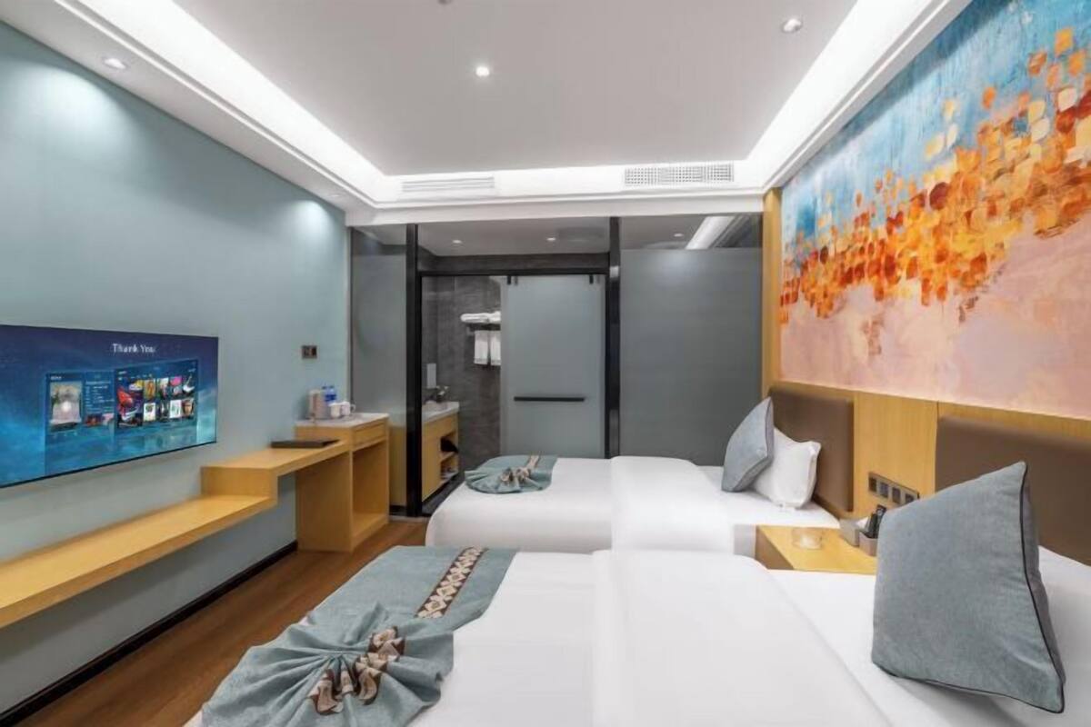 Une chambre d’hôtel moderne avec deux lits, une télévision, un tableau et une salle de bain visible à travers une porte ouverte.