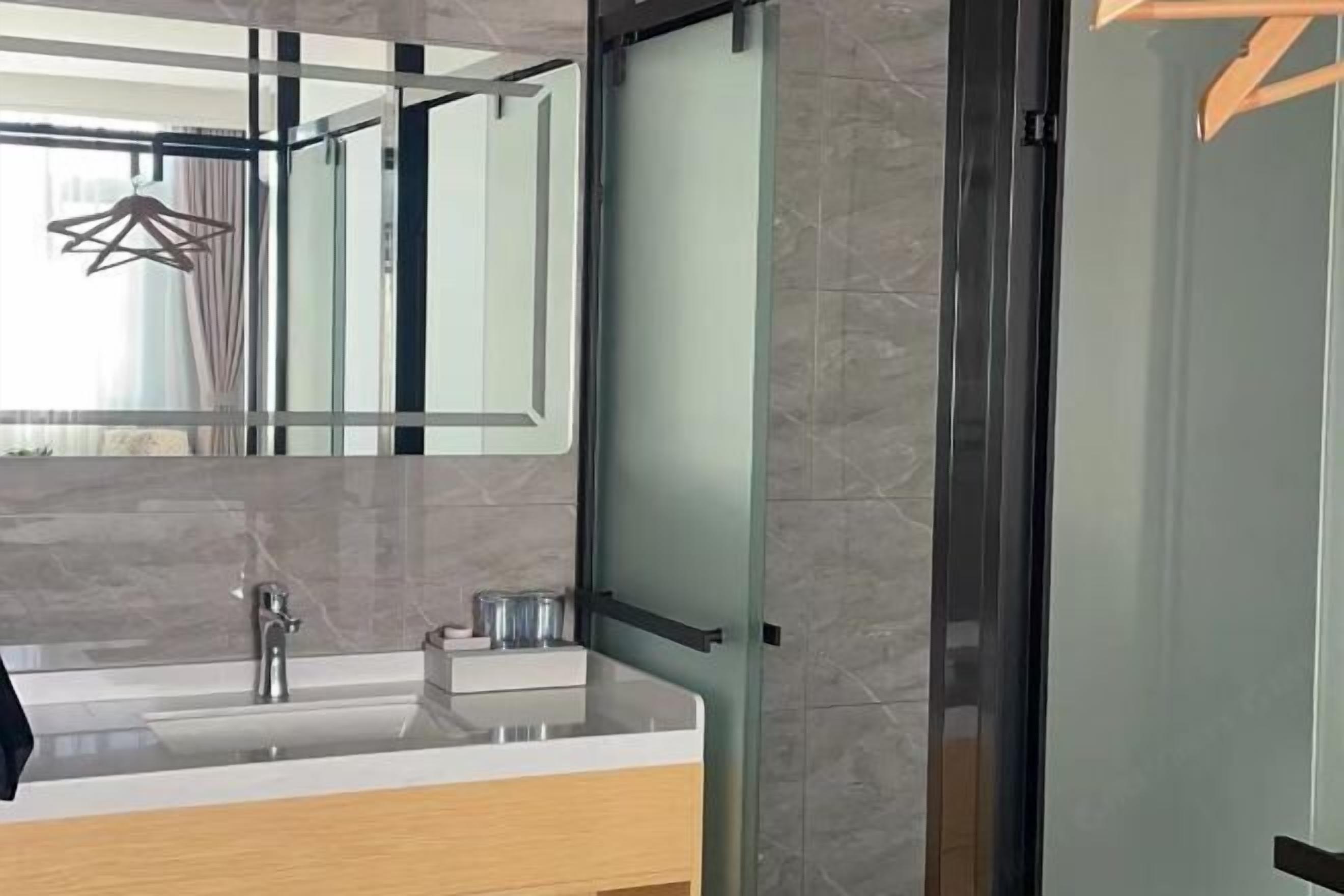 A modern bathroom with a glass-enclosed shower, a white sink with a marble countertop, and a large mirror.
