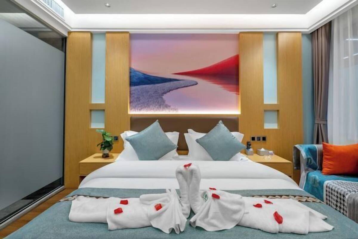 Une chambre d’hôtel avec un grand lit, une table de chevet, une lampe de chevet, un téléviseur fixé au mur et une vue sur un coucher de soleil sur l’eau.