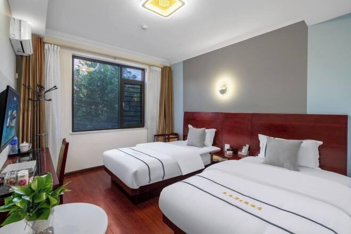 Une chambre d’hôtel avec deux lits, un bureau avec une chaise, une télévision et une fenêtre avec des rideaux.