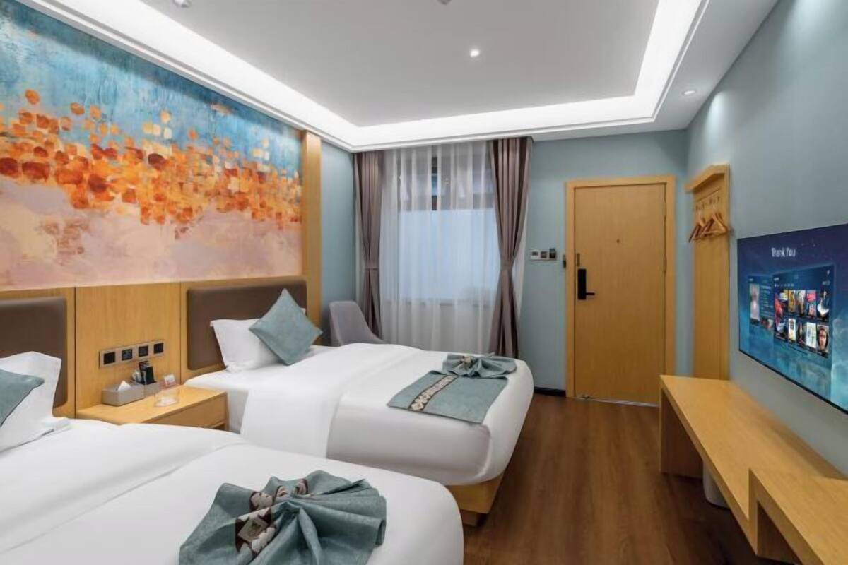 Une chambre d’hôtel avec deux lits, une grande peinture abstraite, un téléviseur et un banc en bois.