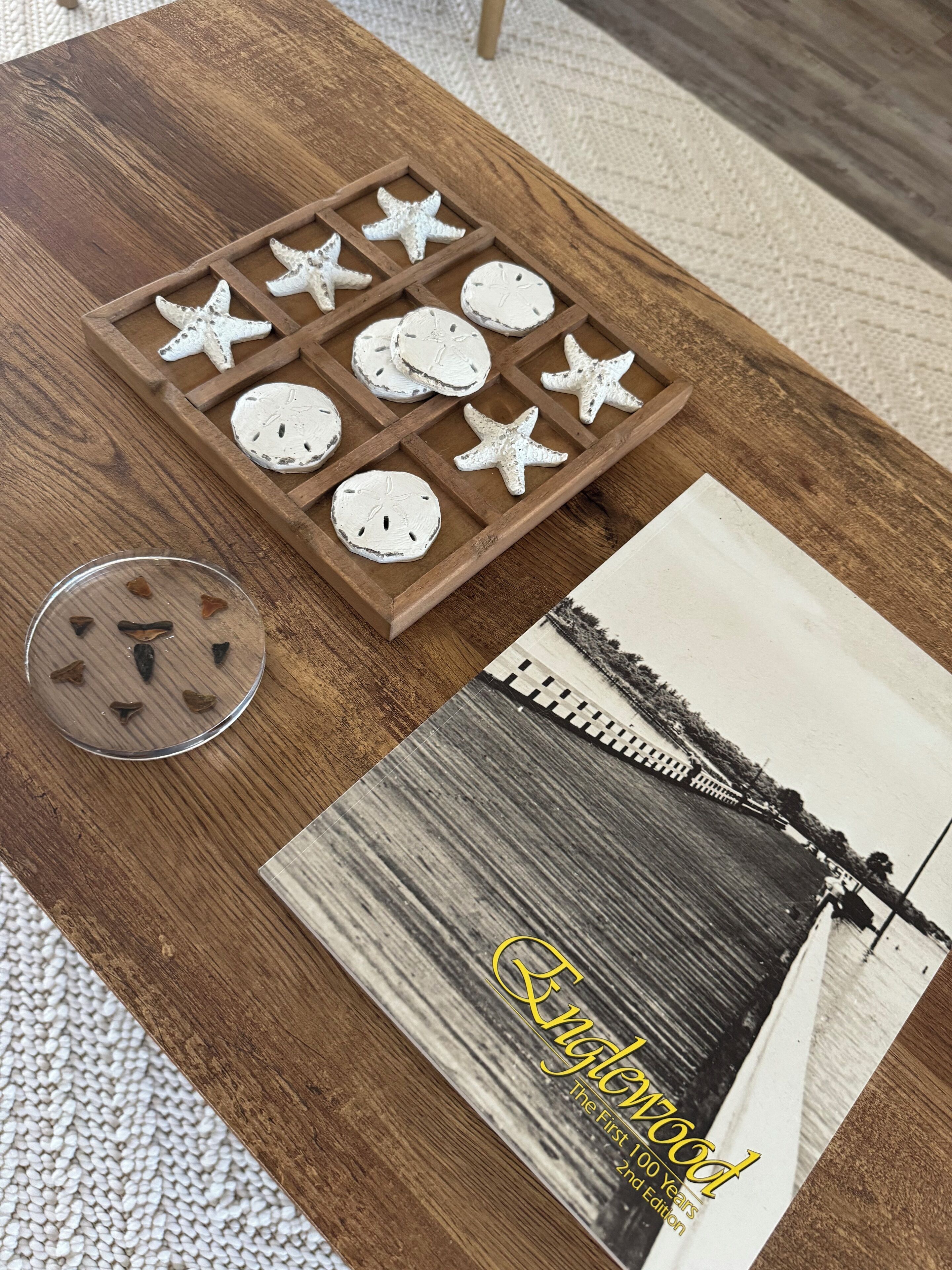 Ein Holztisch mit einem Tablett, Sternfisch und Muscheln, einer Schale mit herzförmigen Gegenständen und einem Buch mit dem Titel 'Kingdom'.