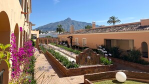 Un cortile con vista sulle montagne, caratterizzato da un vialetto in mattoni, una scultura sferica bianca e un edificio con tetto in tegole.