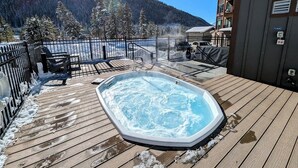 Un jacuzzi en una terraza de madera con vistas a un paisaje nevado y una montaña.