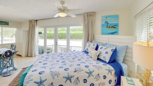 A bedroom with a bed, a ceiling fan, a desk with a chair, and a view of the outdoors. - Walk to Beach: Waterfront Home in Marathon! (Marathon)