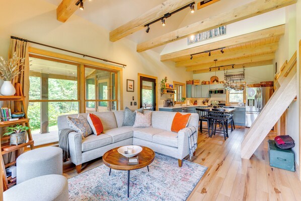 A spacious living room with a large sofa, a coffee table, and a kitchen area visible through an open door.