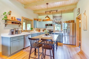 A modern kitchen with wooden cabinets, a central island, stainless steel appliances, and a hanging pot rack.