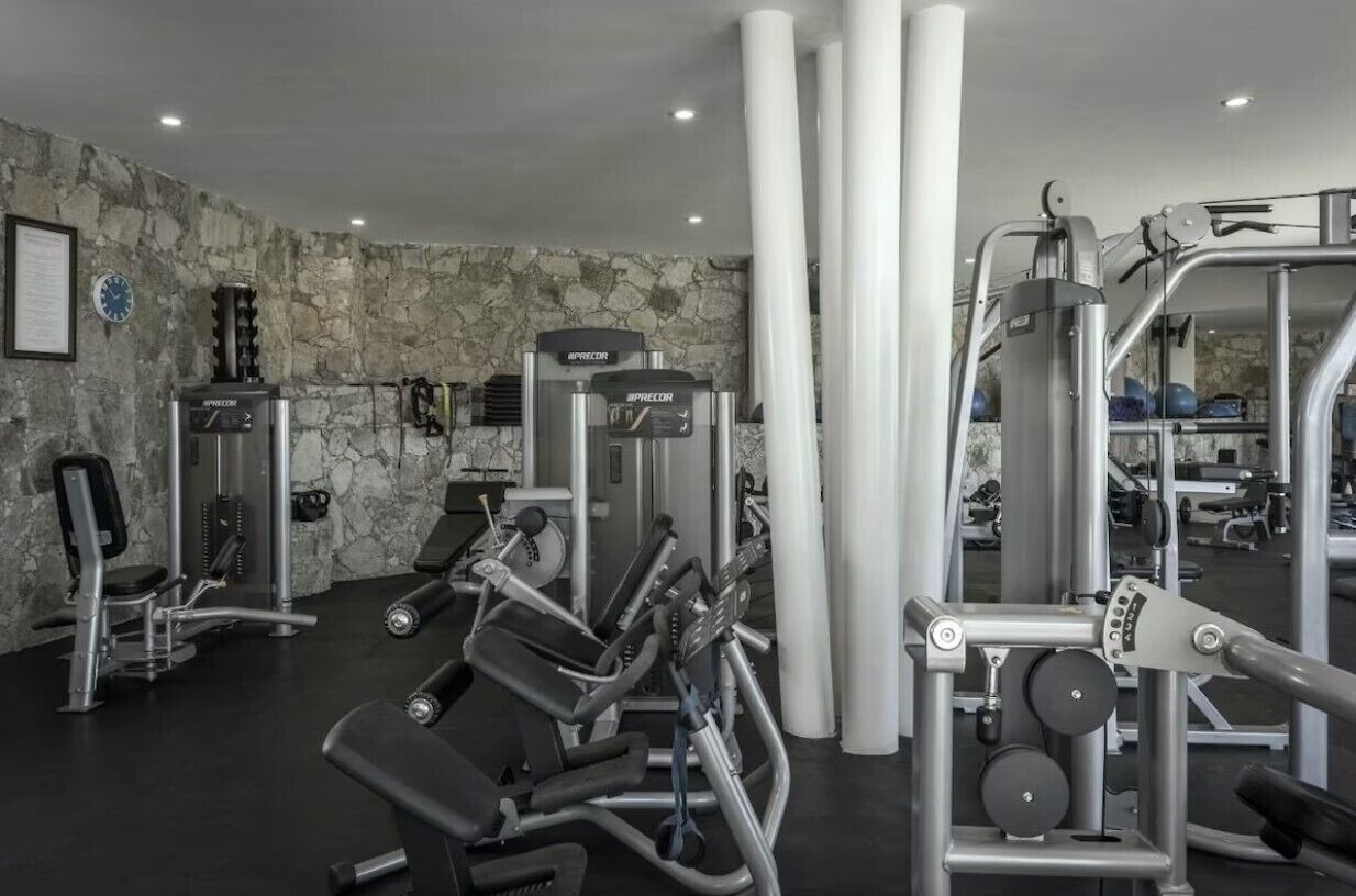 Ein Fitnessstudio mit verschiedenen Trainingsgeräten, einer Steinwand und einer Wanduhr.
