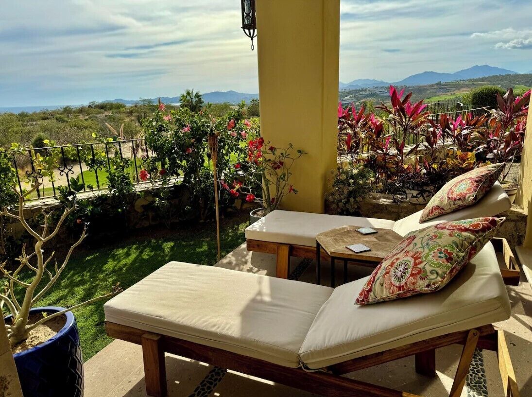 A balcony with a view of a mountainous landscape, a lounge chair, a small table, and potted plants.