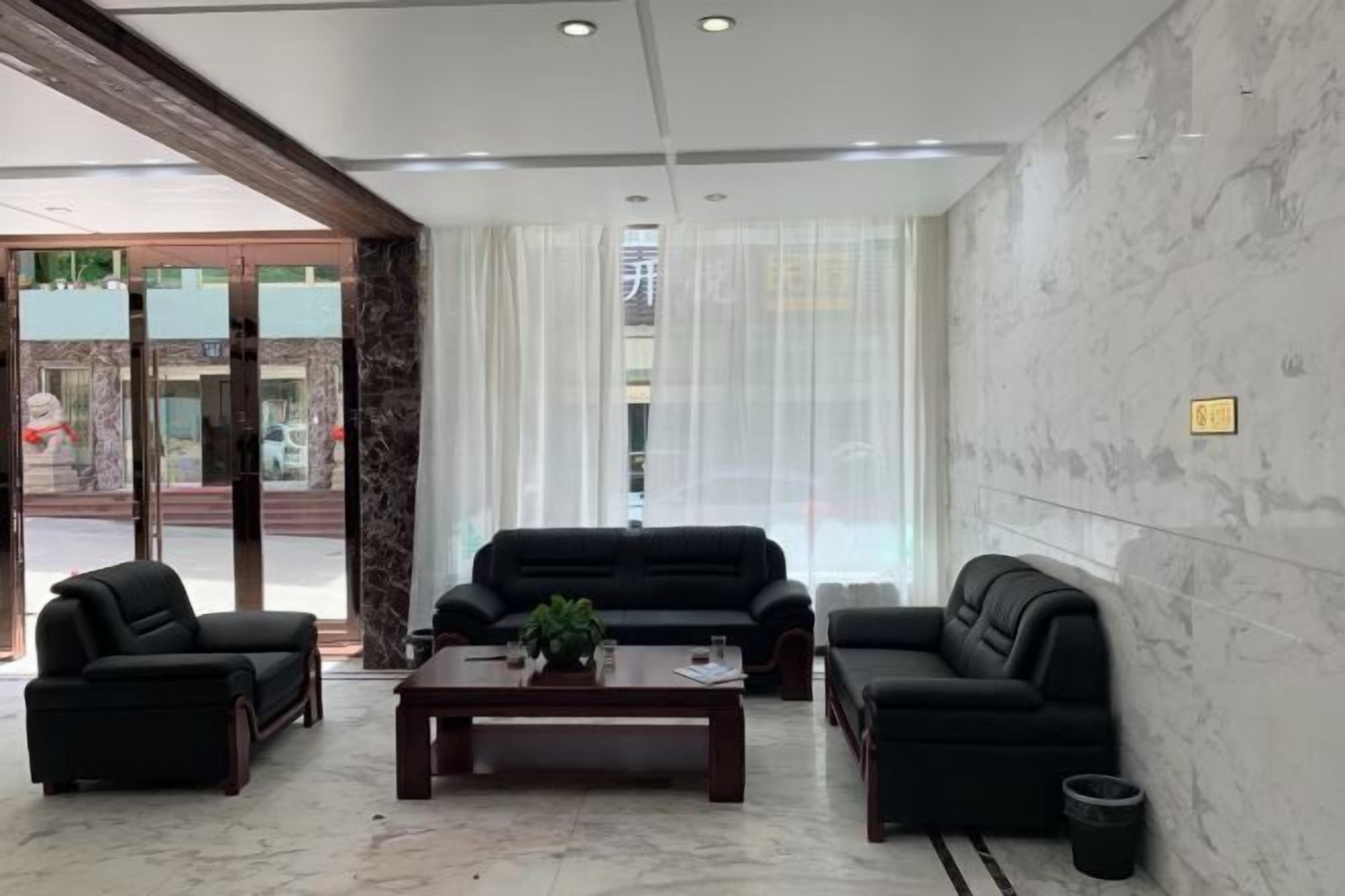 A lobby with a marble floor, black leather sofas, a wooden coffee table, and a glass door entrance.