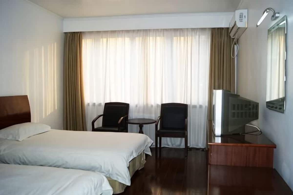 A hotel room with two beds, a desk, two chairs, a TV, and a window with curtains.