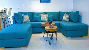 Una sala de estar moderna con un sofá seccional color turquesa, dos mesitas auxiliares y un adorno de pared.