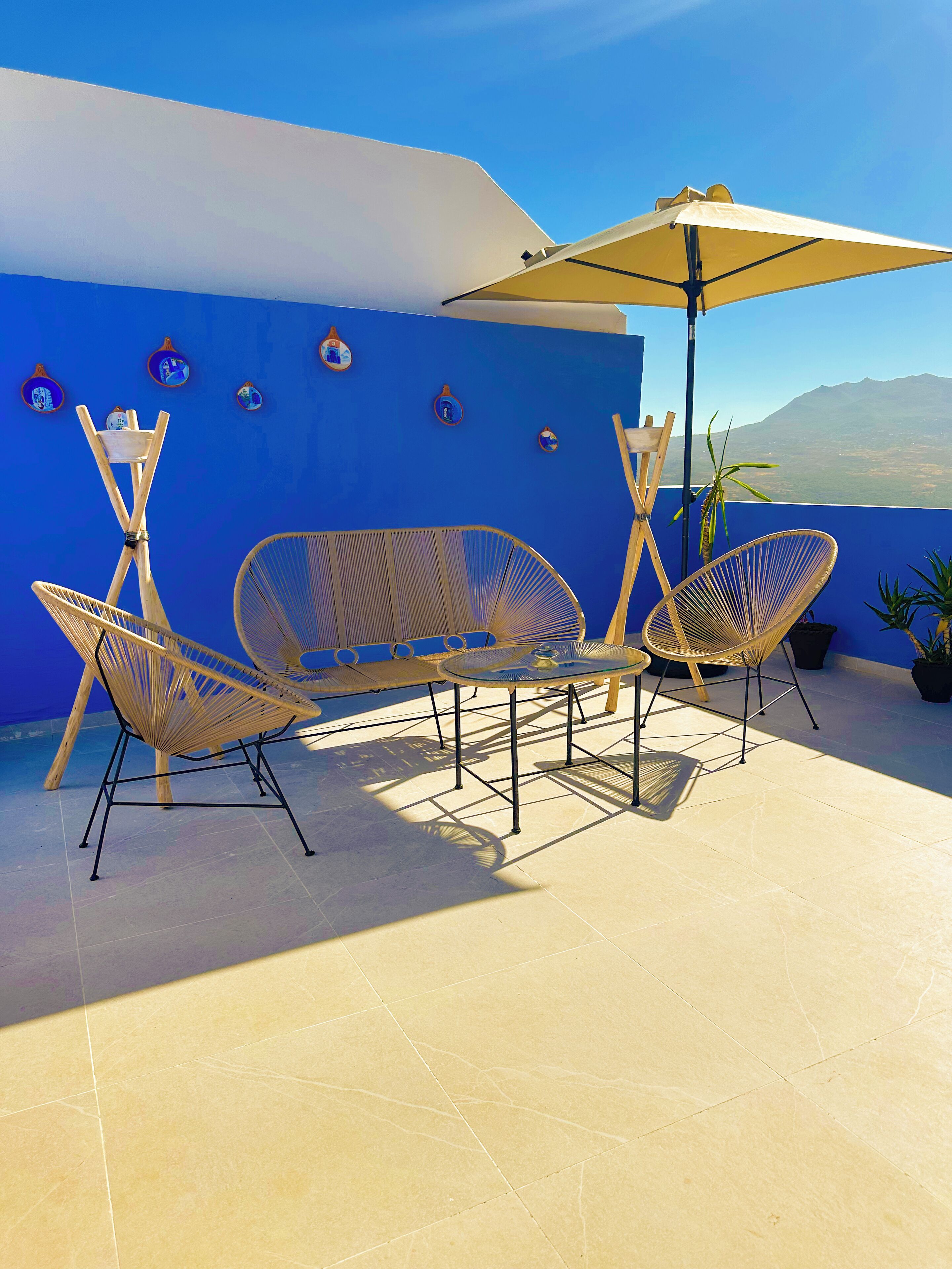 Une terrasse avec deux fauteuils en osier et une table, un parasol jaune et une vue sur une montagne.
