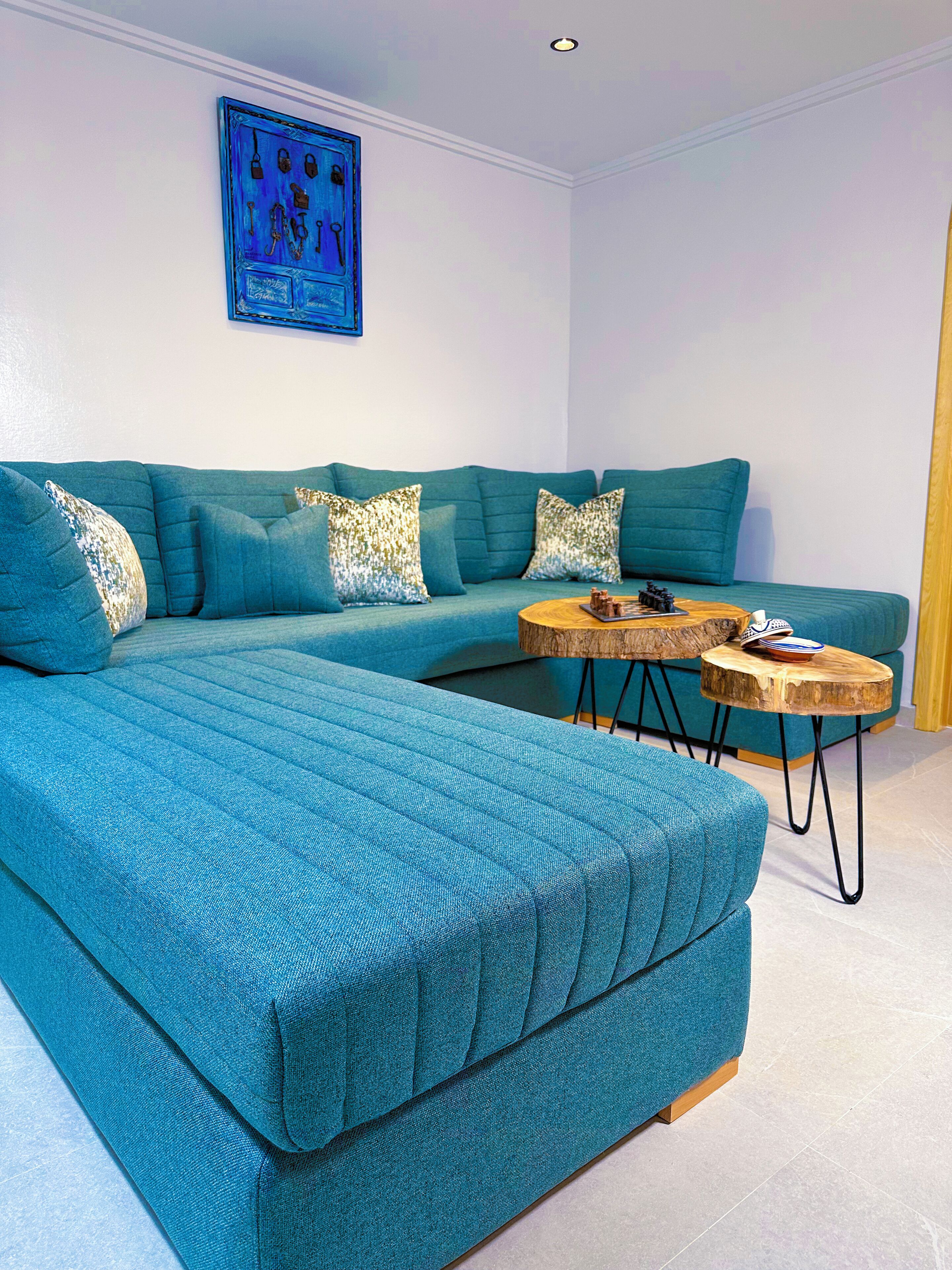 Un canapé d’angle de couleur turquoise avec des coussins à motifs, une table basse en bois et une œuvre d’art accrochée au mur.
